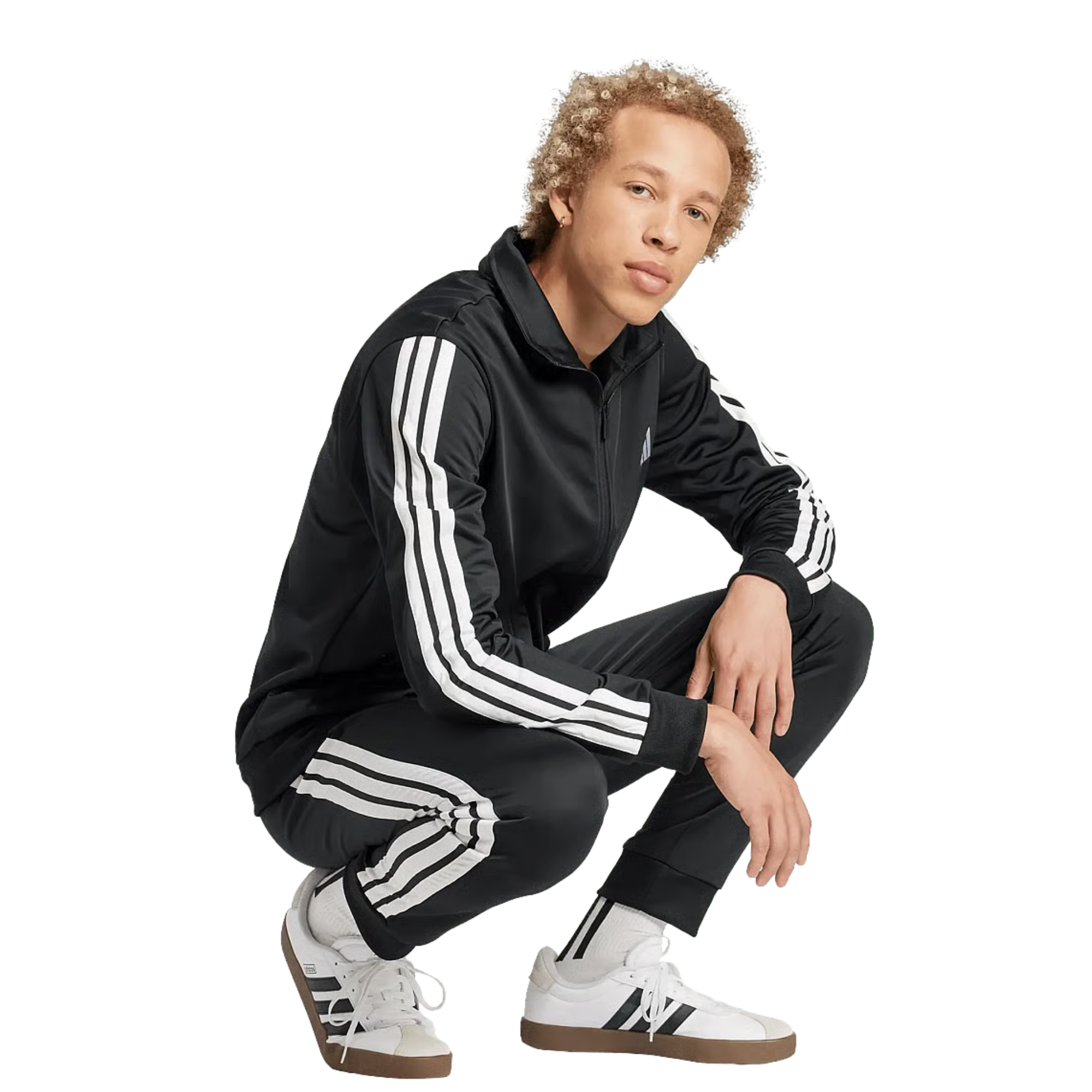 Young man crouching in a black adidas three-stripe tracksuit and white sneakers